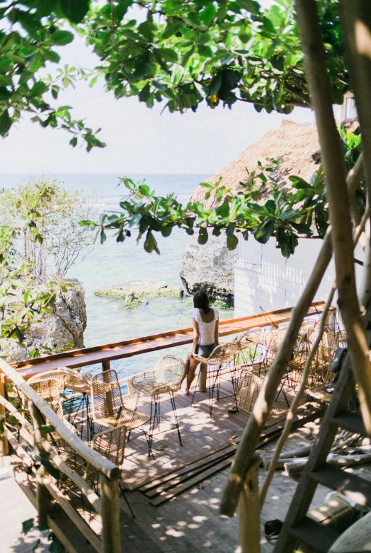 a person standing on a deck next to a body of water, bali, sitting in a cafe, climbing up a cliffside, slide show