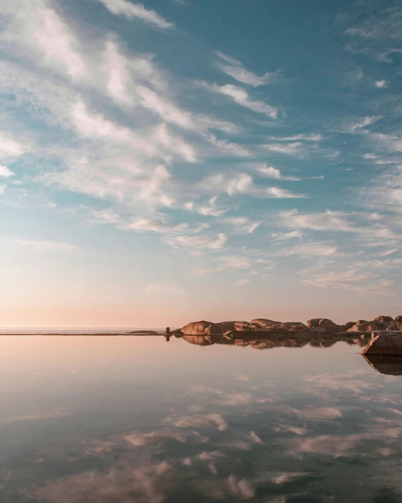 a body of water surrounded by rocks under a cloudy sky, water mirrored water, sherbert sky, looking happy, minimalist