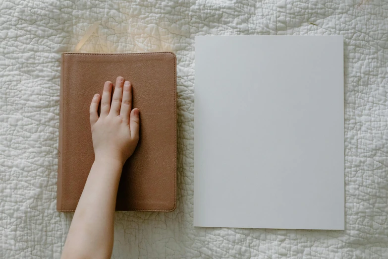 a person laying on a bed next to a book, a minimalist painting, by Carey Morris, unsplash, bump in form of hand, old photobook, kid drawing, ivory and copper