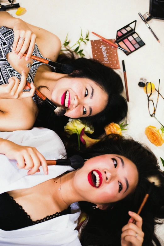 a couple of women laying on top of a bed, inspired by Wang Duo, trending on pexels, putting on lipgloss, half asian, smiling down from above, brown