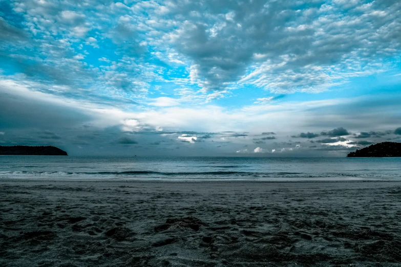 a person standing on a beach under a cloudy sky, shades of blue and grey, oceanside, slide show, landscape photo