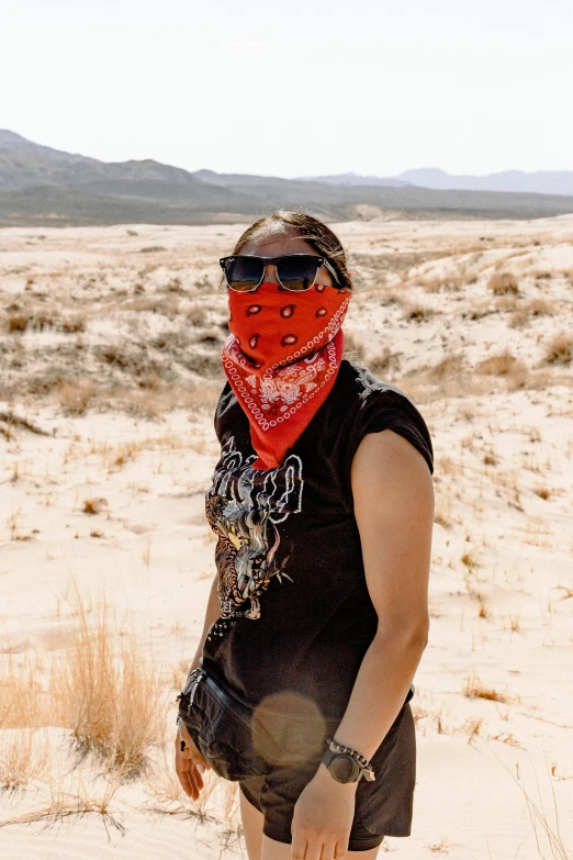 a woman standing in the desert wearing a red bandana, wearing bandit mask, wearing shades, desert setting, taken in the early 2020s