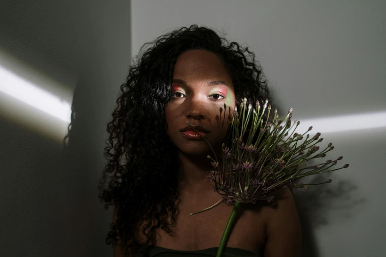 a woman holding a flower in front of her face, an album cover, pexels contest winner, hyperrealism, lights in the dark, mixed-race woman, ( ( dark skin ) ), light room