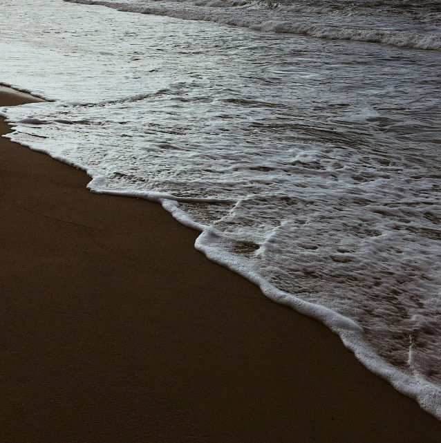 a person walking on a beach next to the ocean, by Elsa Bleda, unsplash, pristine rippling oceanic waves, brown, ignant, laying on beach