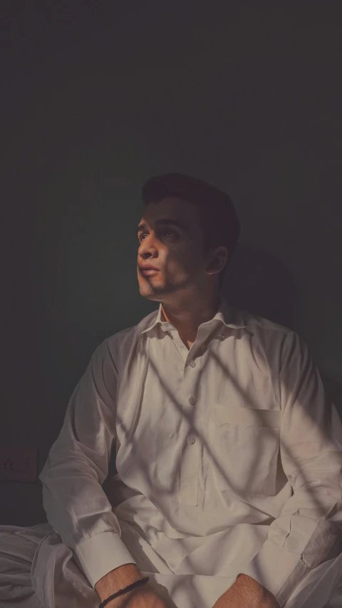 a man sitting on a bed in a dark room, an album cover, inspired by Yousuf Karsh, unsplash, asian man, clear julian lage face, 15081959 21121991 01012000 4k, evening sunlight