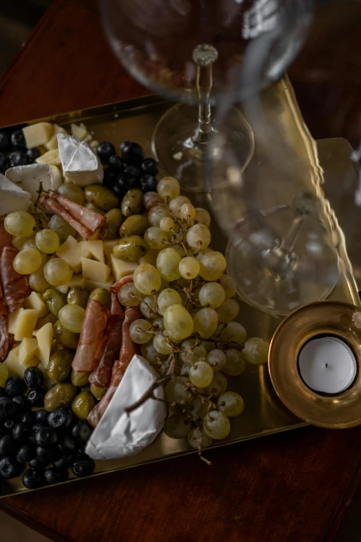 a tray of food sitting on top of a wooden table, a still life, grapes, black and gold palette, bubbly, high quality photo