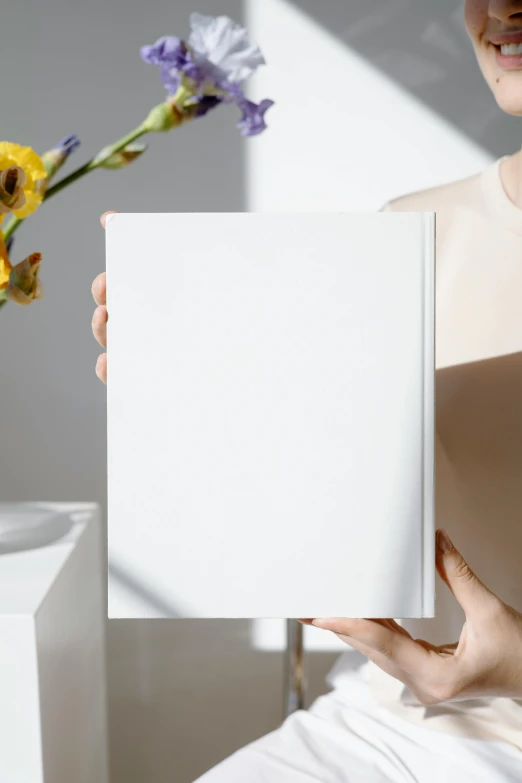 a woman holding a book in front of a vase of flowers, an album cover, trending on pexels, white minimalist architecture, blank paper, white box, product introduction photo