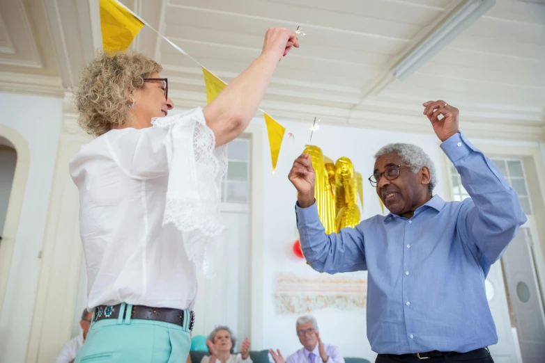 a man and woman holding up balloons in the air, nursing home, white and yellow scheme, community celebration, liquid gold