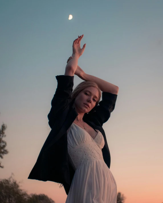 a woman standing on top of a lush green field, an album cover, inspired by Elsa Bleda, unsplash, aestheticism, in front of a pale full moon, doing an elegant pose over you, non binary model, ((sunset))