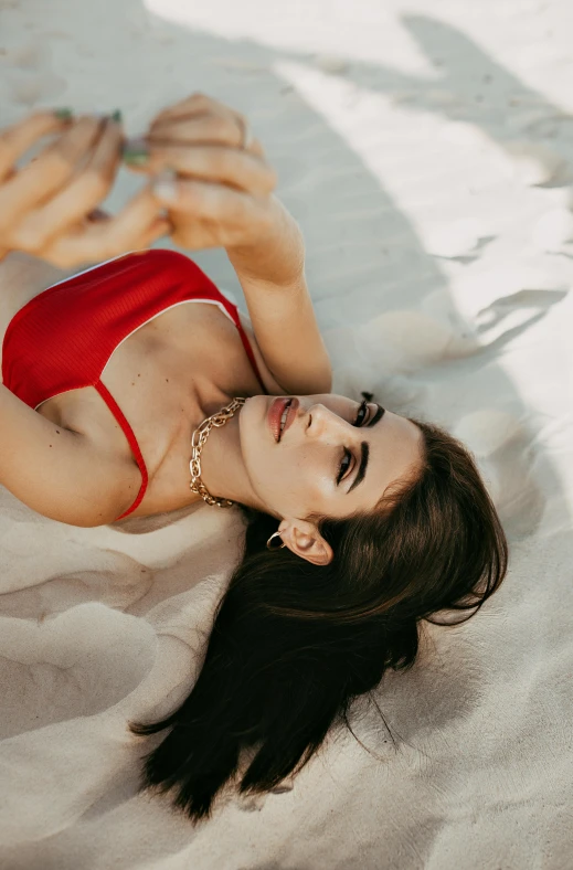 a woman in a red bikini laying in the sand, by Julia Pishtar, trending on pexels, in love selfie, on my bed, gif, brunette