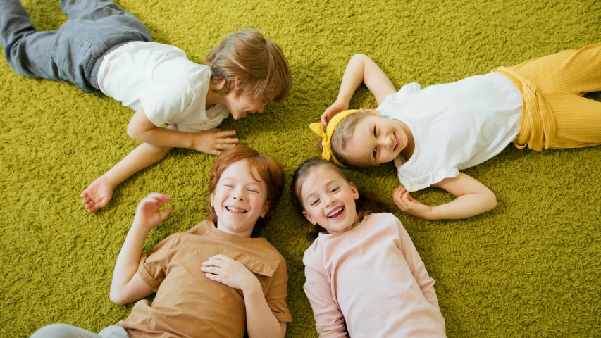 a group of children laying on top of a green carpet, making the best smug smile, rugs, 15081959 21121991 01012000 4k, thumbnail