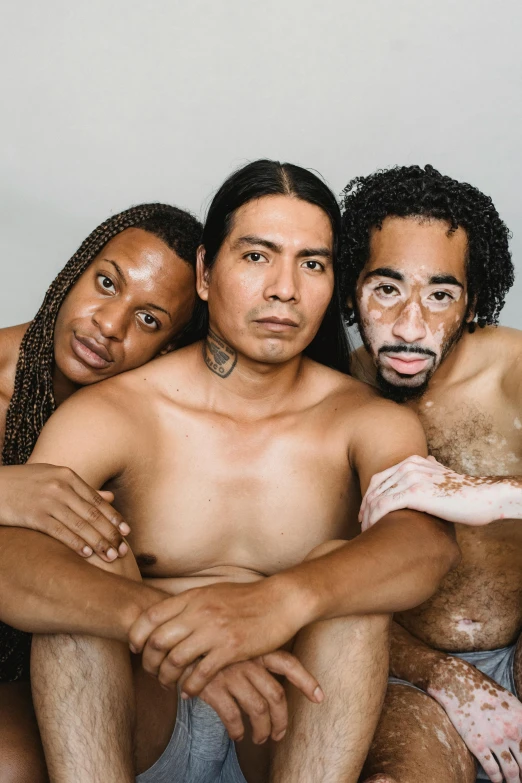 a group of people sitting on top of a bed, an album cover, by Jessie Alexandra Dick, unsplash, renaissance, three hairy neanderthal people, latino features, muscular men entwined together, 3 actors on stage