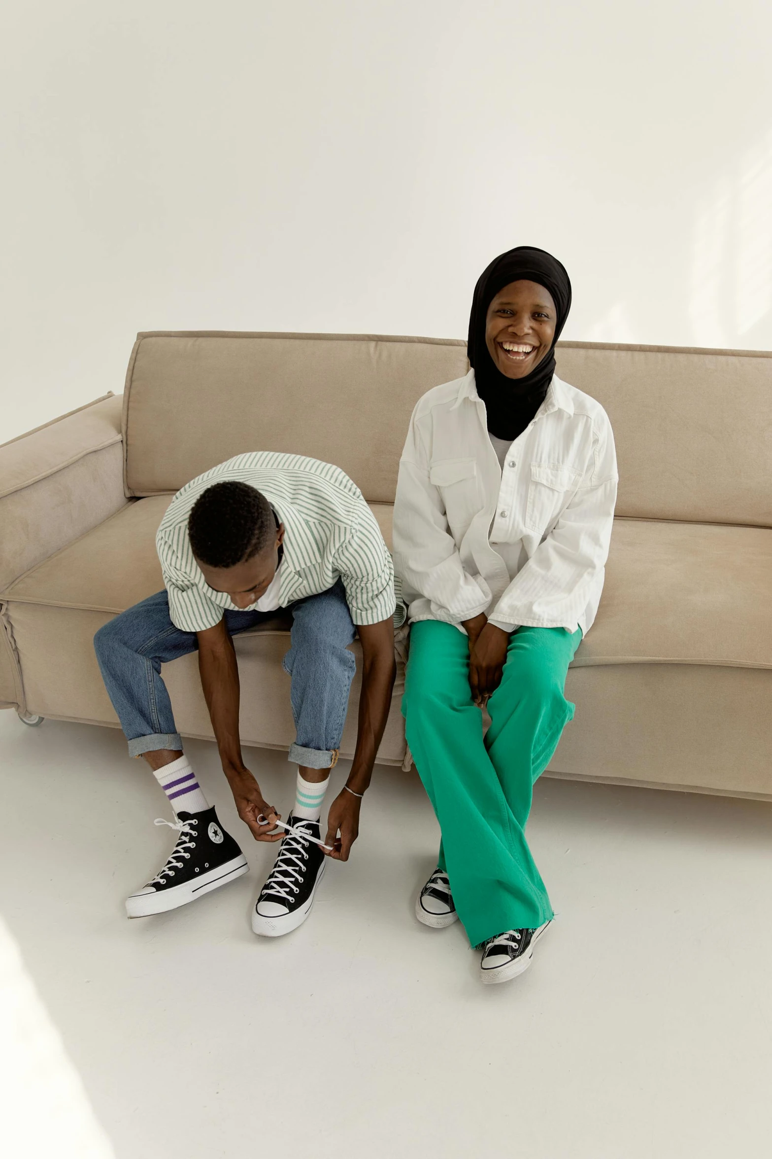 a couple of people sitting on top of a couch, trending on pexels, hurufiyya, wearing pants, riyahd cassiem, genderless, wearing white sneakers