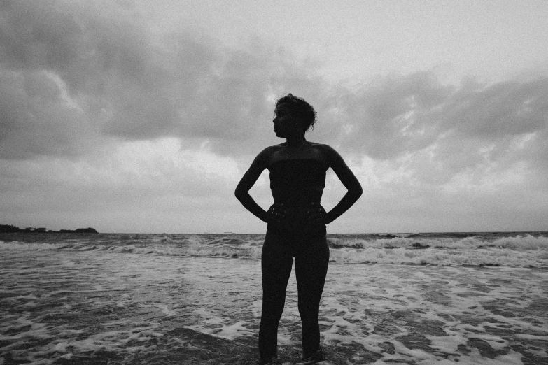 a black and white photo of a woman standing in the ocean, pexels, black girl, female cyborg black silhouette, on a cloudy day, homemade