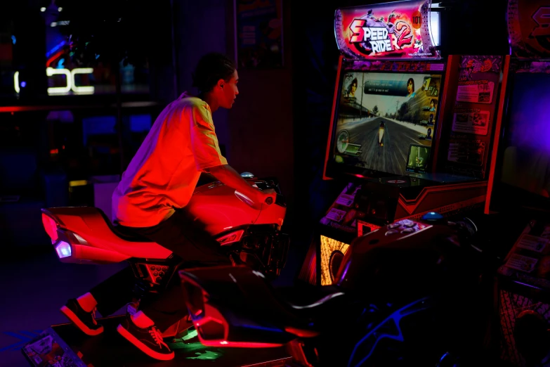 a man sitting on a motorcycle playing a video game, by Meredith Dillman, pexels, neogeo, dive bar with a karaoke machine, neon lights and adds, ap, action sports