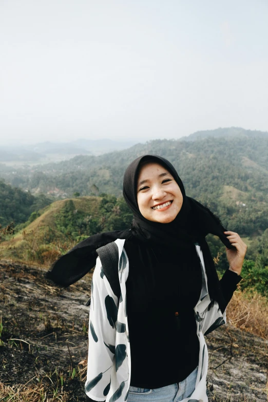 a woman standing on top of a rocky hill, a picture, inspired by JoWOnder, unsplash, sumatraism, wearing a head scarf, smiling slightly, low quality photo, ((portrait))