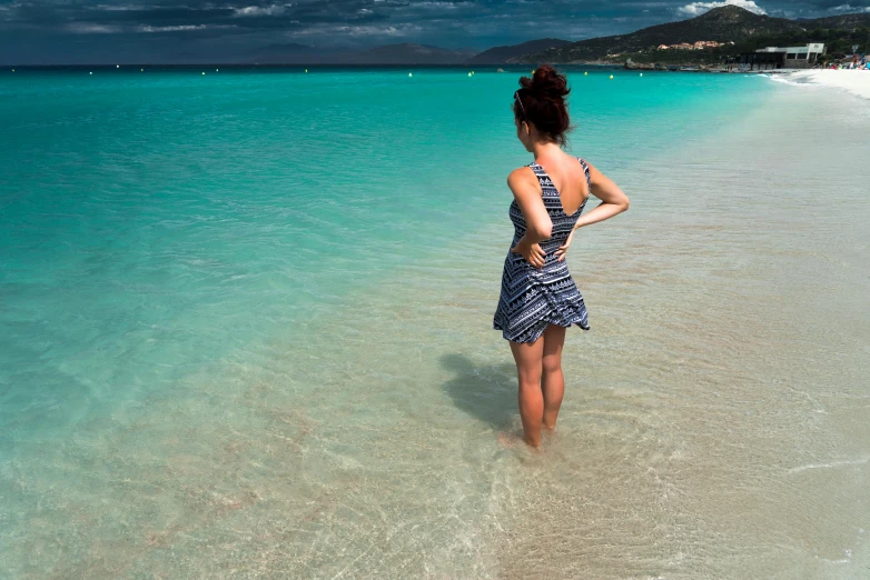 a woman standing on top of a beach next to the ocean, a photo, inspired by Henri-Edmond Cross, pexels contest winner, arabesque, carribean turquoise water, standing in the isle of harris, looking from behind, dress made of water