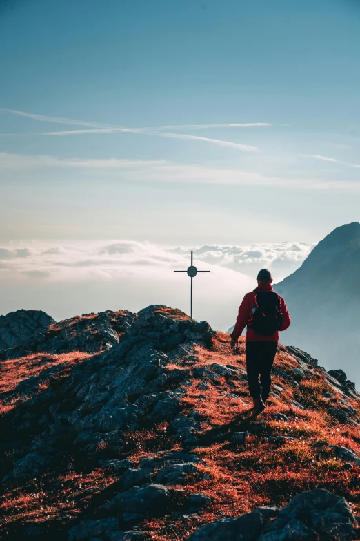 a person standing on top of a mountain with a cross in the background, walking away from camera, wearing adventure gear, alps, multiple stories