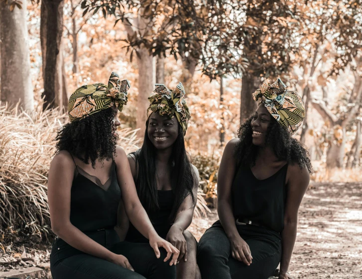 a group of three women sitting next to each other, by Ingrida Kadaka, pexels contest winner, afrofuturism, vine headdress, trees in background, black, ebony