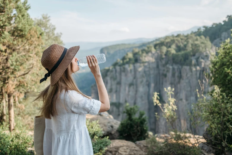 a woman in a hat drinking water from a bottle, pexels contest winner, renaissance, gorge in the mountain, al fresco, rocky cliff, an australian summer landscape