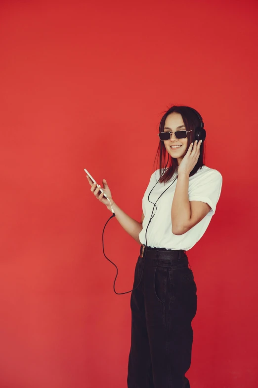 a woman standing in front of a red wall talking on a cell phone, an album cover, trending on pexels, headphones dj rave, brunette, plain background, scientific