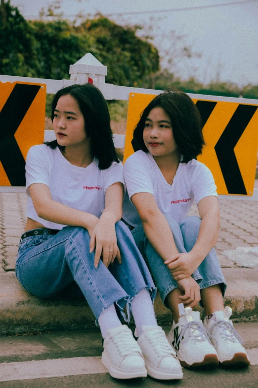 a couple of women sitting next to each other, a picture, inspired by Wang Duo, trending on pexels, wearing a t-shirt, standing in road, promotional image, young asian girl