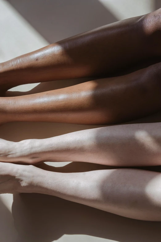 a couple of legs sitting next to each other, trending on pexels, skin tones, they are all laying down, skincare, long cast shadows