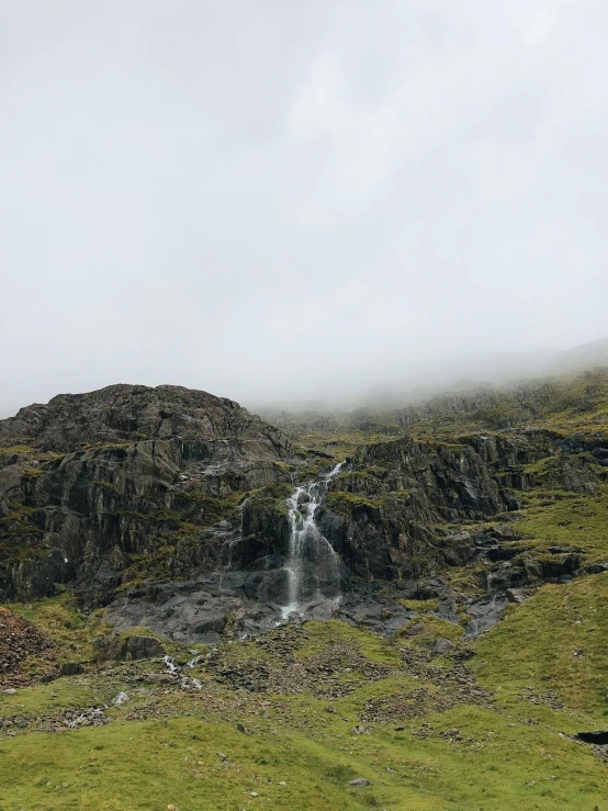 a herd of sheep standing on top of a lush green hillside, standing in a waterfall, with lots of dark grey rocks, misty and eerie, lariennechan