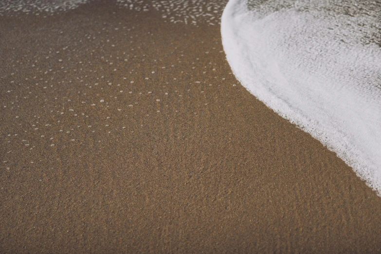 a white surfboard sitting on top of a sandy beach, a stipple, inspired by Andreas Gursky, unsplash, foamy bubbles, powder, brown water, curving