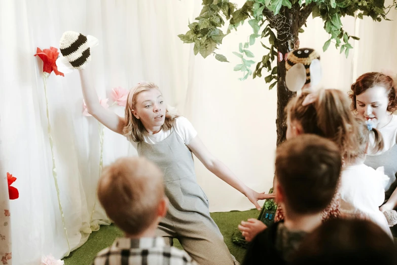 a group of children sitting in front of a tree, a cartoon, inspired by Elsa Beskow, unsplash, interactive art, tickle fight in the death tent, giant ferret, indoor scene, in an action pose