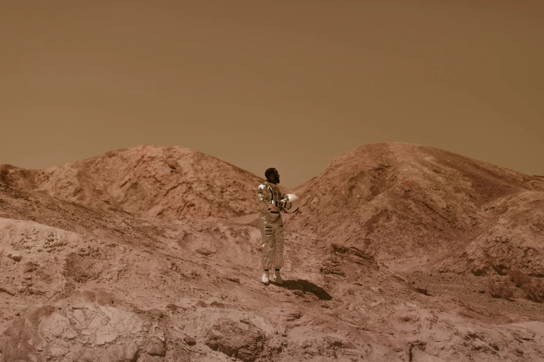 a man standing on top of a rocky hill, an album cover, inspired by Mike Winkelmann, pexels contest winner, afrofuturism, woman astronaut, sepia colors, standing with her back to us, on mars