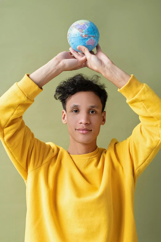 a young man holding a globe above his head, pexels contest winner, nonbinary model, yellow and blue, varying ethnicities, wearing a light blue shirt