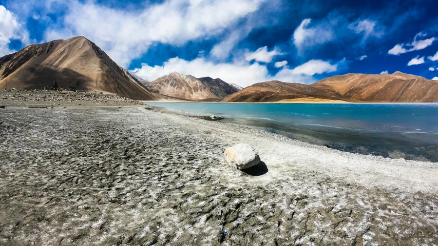 a large body of water with mountains in the background, by Julia Pishtar, pexels contest winner, land art, breathtaking himalayan landscape, blue sand, stones falling from the sky, conde nast traveler photo