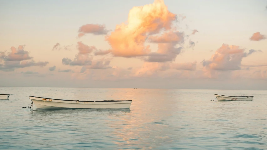 a couple of boats floating on top of a body of water, by Alison Geissler, unsplash contest winner, romanticism, light pink clouds, jamaica, ignant, skiff