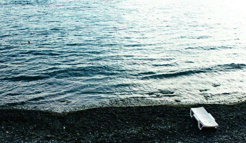 a chair sitting on top of a beach next to a body of water, an album cover, inspired by Elsa Bleda, unsplash, minimalism, black sand, rinko kawauchi, inlets, seattle