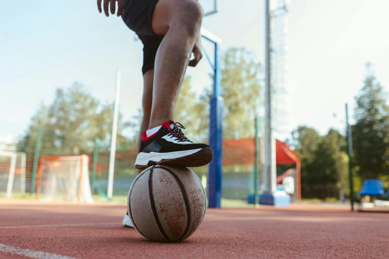 a man standing on top of a basketball ball on a court, trending on dribble, wearing red shorts, outside on the ground, thumbnail, local gym