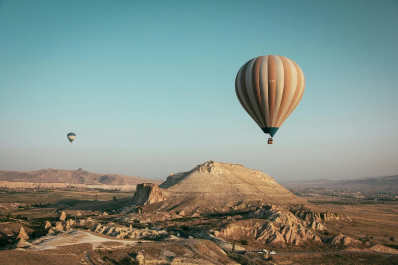 a couple of hot air balloons flying over a valley, by Daren Bader, pexels contest winner, beige, turkish and russian, in the style wes anderson, conde nast traveler photo