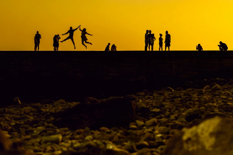 a group of people standing on top of a rocky beach, by Peter Churcher, pexels contest winner, art photography, warm golden backlit, horizontally leaping!!!, families playing, yellow