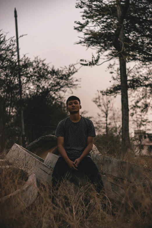 a man sitting in a field next to a tree, an album cover, unsplash, sumatraism, asian male, standing in a dimly lit room, outdoor photo, looking straight