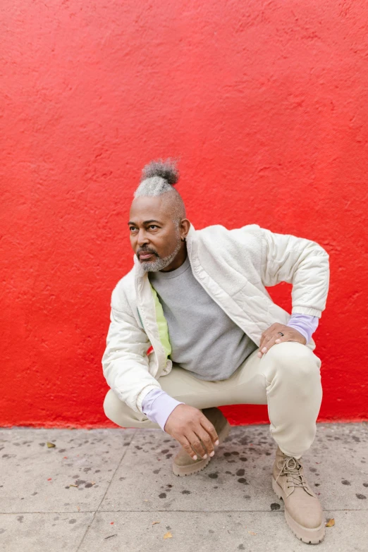 a man squatting in front of a red wall, black arts movement, grey mustache, wearing a track suit, j. h. williams iii, doing a sassy pose