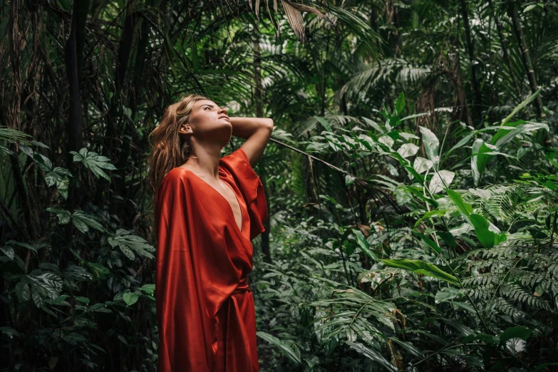 a woman in a red dress standing in a forest, trending on unsplash, in the background is lush jungle, wearing a luxurious silk robe, avatar image, tourist photo