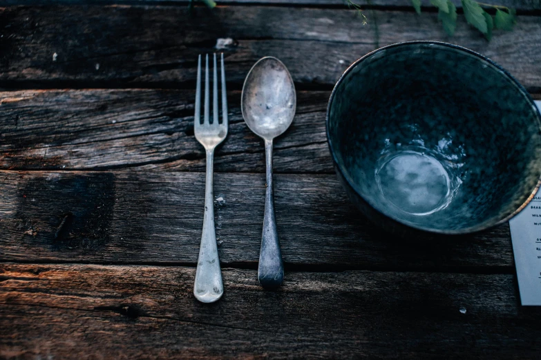 a blue bowl sitting on top of a wooden table, a still life, unsplash, silver，ivory, fork, aged, long