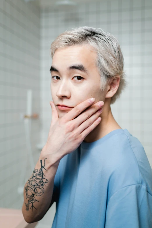 a man that is standing in front of a mirror, an album cover, inspired by jeonseok lee, hyperrealism, with blue hair, skincare, hand on his cheek, surgeon