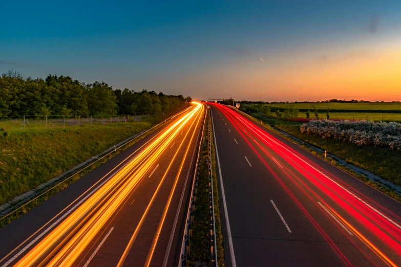 a highway filled with lots of traffic next to a lush green field, by Thomas Häfner, pexels contest winner, orange and red lighting, golden and blue hour, speed, thumbnail