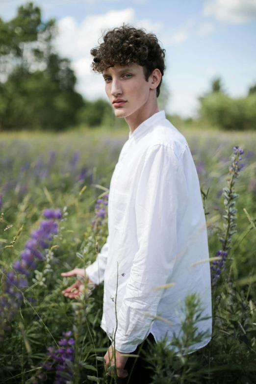 a man standing in a field of purple flowers, an album cover, inspired by Raphaël Collin, unsplash, renaissance, wearing a white button up shirt, model posing, androgyny, valentin serov style