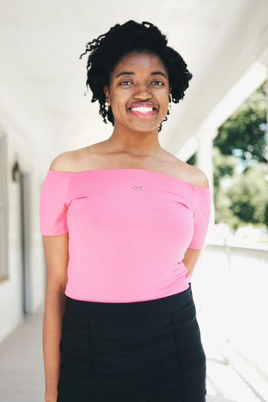 a woman in a pink top and black skirt, by Dulah Marie Evans, dark short curly hair smiling, off the shoulder shirt, academic clothing, vp of marketing