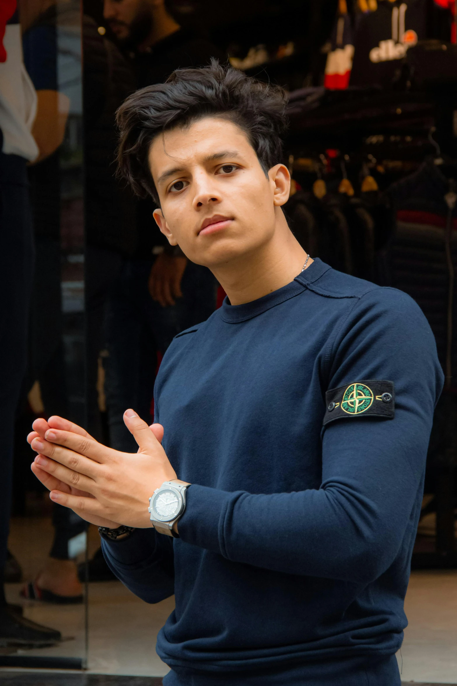 a young man standing in front of a store, inspired by Carlos Berlanga, instagram, renaissance, in a navy blue sweater, wearing a watch, london gang member, official store photo