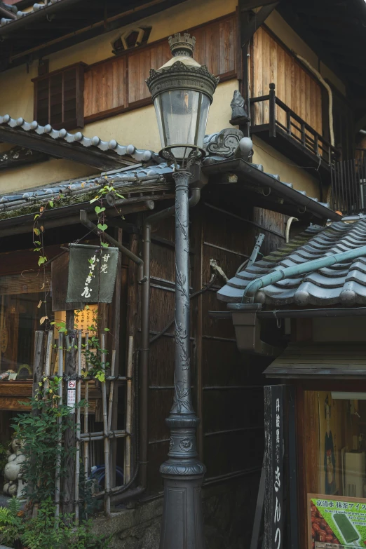 a street light sitting on the side of a building, inspired by Watanabe Shōtei, peaked wooden roofs, old town, lush surroundings, wrought iron architecture