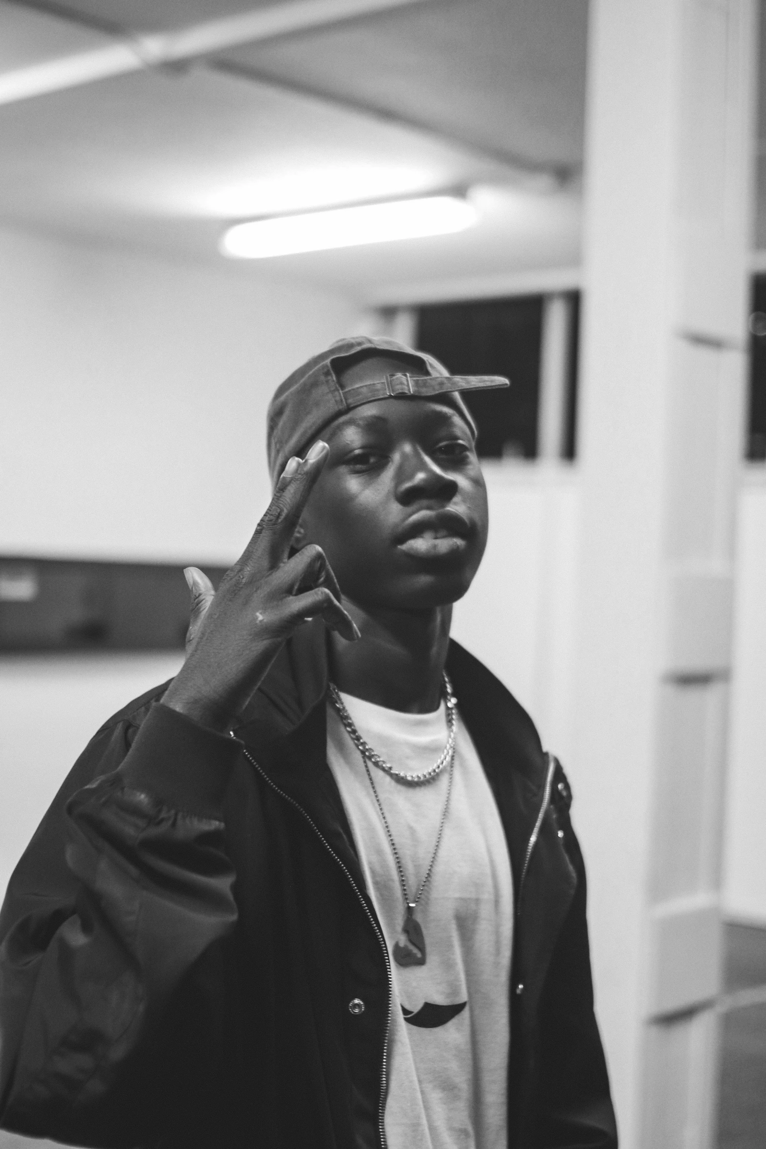 a black and white photo of a man talking on a cell phone, an album cover, by Bascove, trending on pexels, realism, black teenage boy, smol, he is wearing a hat, lights off