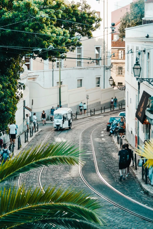 a group of people walking down a street next to tall buildings, the city of lisbon, lush surroundings, tram, flatlay